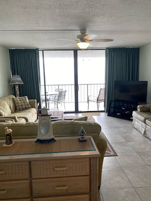 Relax in this stylish living room with a sofa set, ceiling fan, and large window offering a view of the outdoor balcony with dining area.