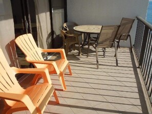En balkon med orange plastikstole, et træbord og et lille rundt bord med stole.