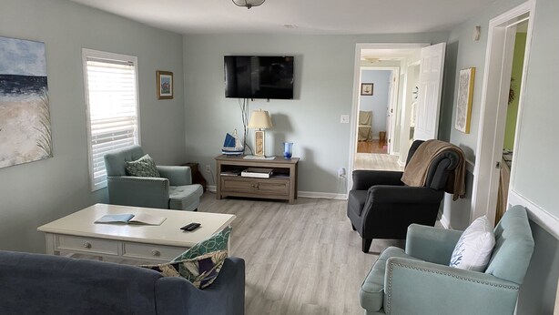 A living room with a flat-screen TV, two sofas, a coffee table, and a side table with decorative items. - One Street Over - Cottage by the Sea! (Carolina Beach)