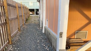 A gravel pathway leading to a building entrance with a wooden fence on one side and a garage door on the other. - One Street Over - Cottage by the Sea! (Carolina Beach)