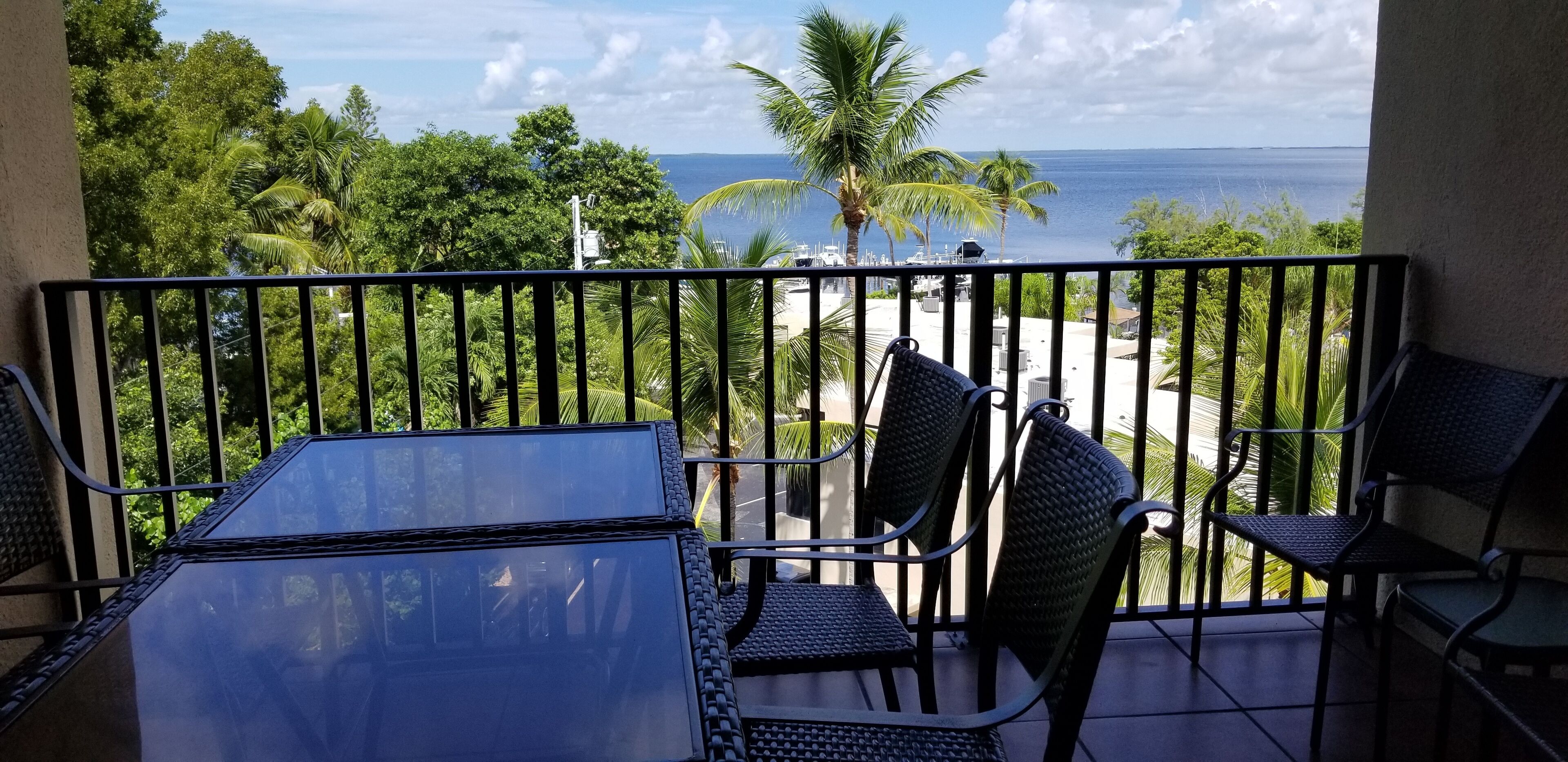Un balcón con mesa y sillas, con vista al mar y palmeras.