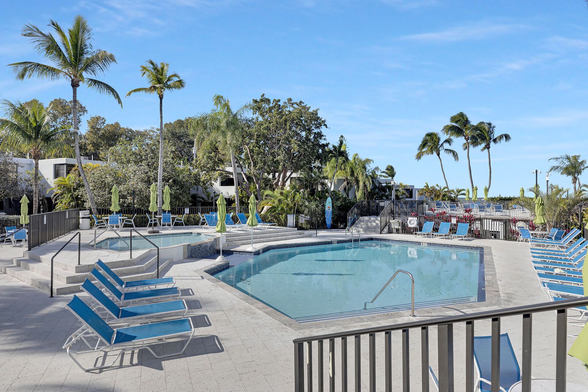 A pool area with blue lounge chairs, a clear pool, and palm trees.