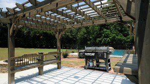 Une pergola en bois avec un barbecue et une piscine en arrière-plan.