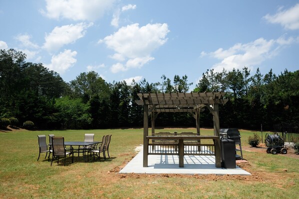 An outdoor patio area with a pergola, dining table, chairs, and a grill. - Mansion stay for big groups 8 miles from LakePoint Sports! (Acworth)