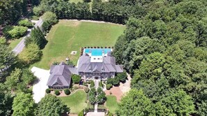 Une grande maison à plusieurs étages, dotée d’une piscine et entourée d’une végétation luxuriante.