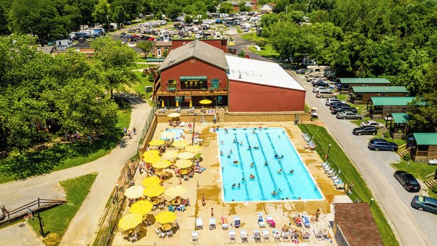 Uma piscina grande com várias pistas de natação, rodeada por espreguiçadeiras e guarda-sóis, com um edifício ao fundo.
