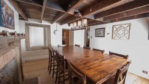 Uma sala de jantar espaçosa com uma longa mesa de madeira e cadeiras, teto rústico e parede de tijolos.