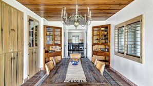 A dining room with a wooden table, chairs, and a chandelier. There are cabinets with glass doors and a window with blinds. - Luxury Adobe in Wine Country w/ Pool, Hot Tub & Ping-Pong, 10 min from downtown (Paso Robles)