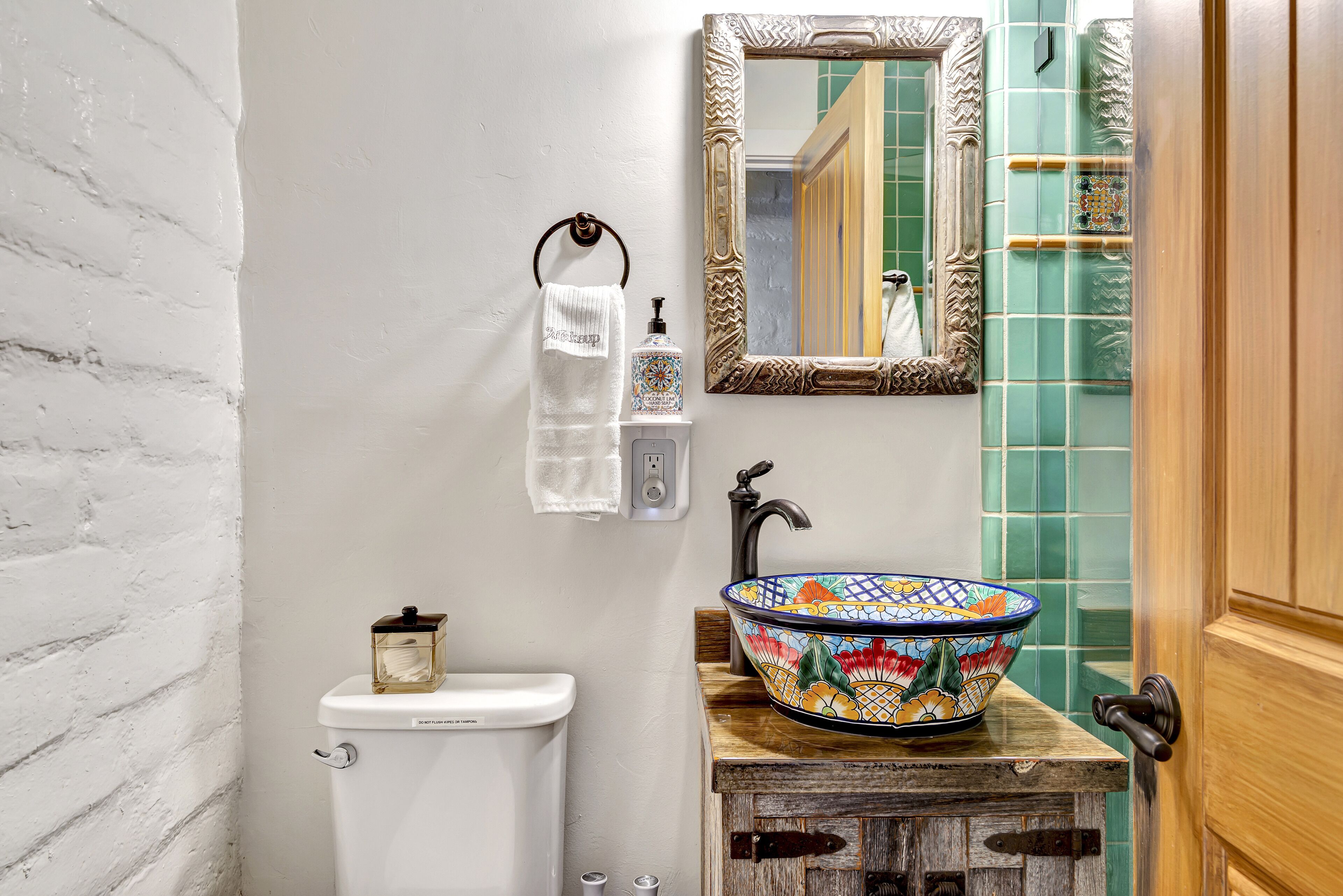 A bathroom with a white toilet, a wooden sink with a colorful bowl, a towel rack with a white towel, and a mirror with an ornate frame.
