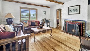 A living room with a fireplace, wooden furniture, and a white brick wall. - Luxury Adobe in Wine Country w/ Pool, Hot Tub & Ping-Pong, 10 min from downtown (Paso Robles)