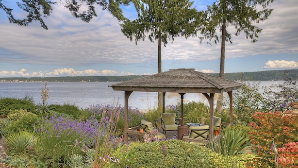 A gazebo with seating, surrounded by a garden with various plants and flowers, overlooking a body of water. - Serene getaway close to the beach with garden for couples or solo adventurers  (Port Hadlock-Irondale)
