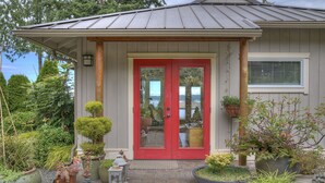 A house with a red door, a porch with potted plants, and a view of the surrounding greenery. - Serene getaway close to the beach with garden for couples or solo adventurers  (Port Hadlock-Irondale)