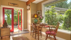 A dining area with a wooden table, chairs, a vase with flowers, and a window with a view of greenery. - Serene getaway close to the beach with garden for couples or solo adventurers  (Port Hadlock-Irondale)