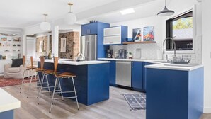 A modern kitchen with blue cabinetry, a central island, bar stools, and a large window. - River's Edge (Leland)