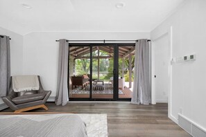 A modern bedroom with a large sliding glass door leading to an outdoor patio. - River's Edge (Leland)