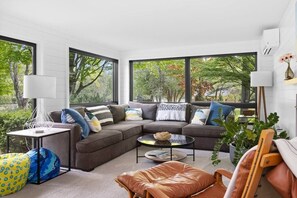 A modern living room with a sectional sofa, a coffee table, and a view of trees through large windows.
