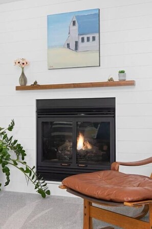 A fireplace with a mantel shelf, a chair, and a painting above the fireplace. - River's Edge (Leland)
