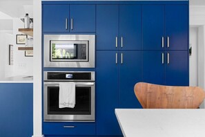 A modern kitchen with blue cabinets, stainless steel appliances, and a wooden chair. - River's Edge (Leland)