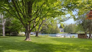 A grassy area with a large tree, a lake, and boats docked. - River's Edge (Leland)