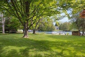A grassy area with a large tree, a lake, and boats docked.