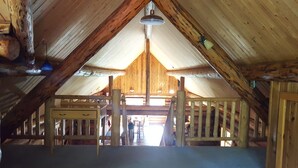 Habitación en ático con techo inclinado, vigas de madera y una lámpara central.