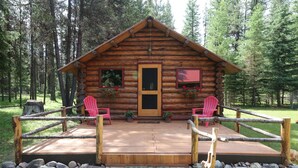 Una cabaña de troncos con una terraza de madera, dos sillas Adirondack rojas y un sendero de piedra que lleva a la puerta.