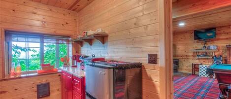 A cabin interior with a kitchen area featuring red cabinets, a stainless steel refrigerator, and a window with a view of greenery.