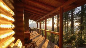 Um deck de madeira com bancos, com vista para uma área arborizada e uma montanha ao fundo.