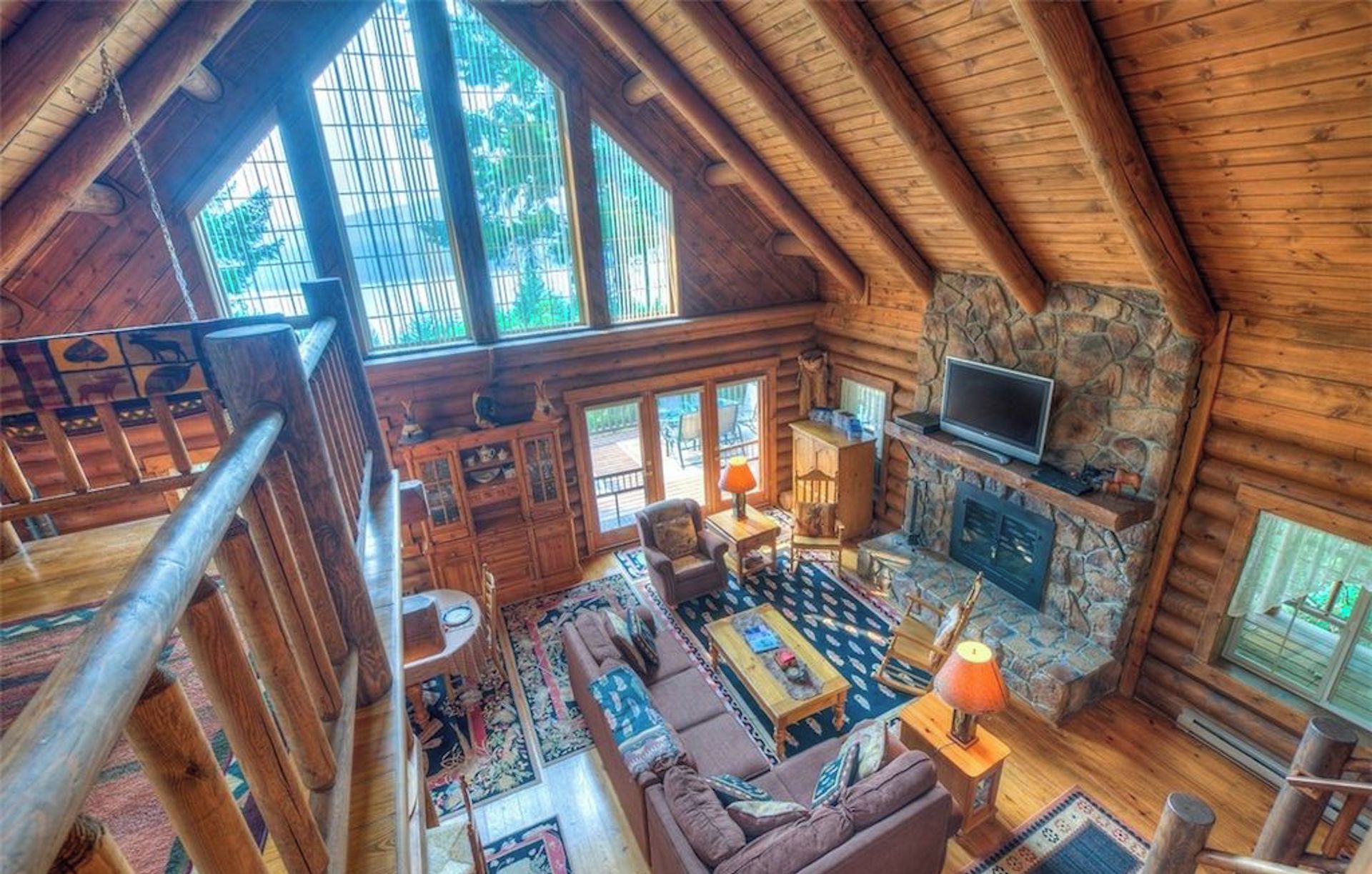 L’intérieur d’une cabane en rondins, avec une cheminée en pierre, un téléviseur et une grande fenêtre donnant sur un paysage verdoyant.