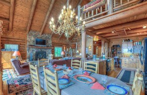 A rustic cabin interior with a dining area, a fireplace, and a television. - Timber Lodge Log Home, 10 Person Theater Room, Hot Tub, Pool Table, Ocean Views! (Orcas Island)