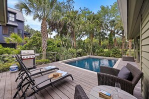 Un área junto a la piscina con sillones de descanso, una parrilla y una terraza de madera.