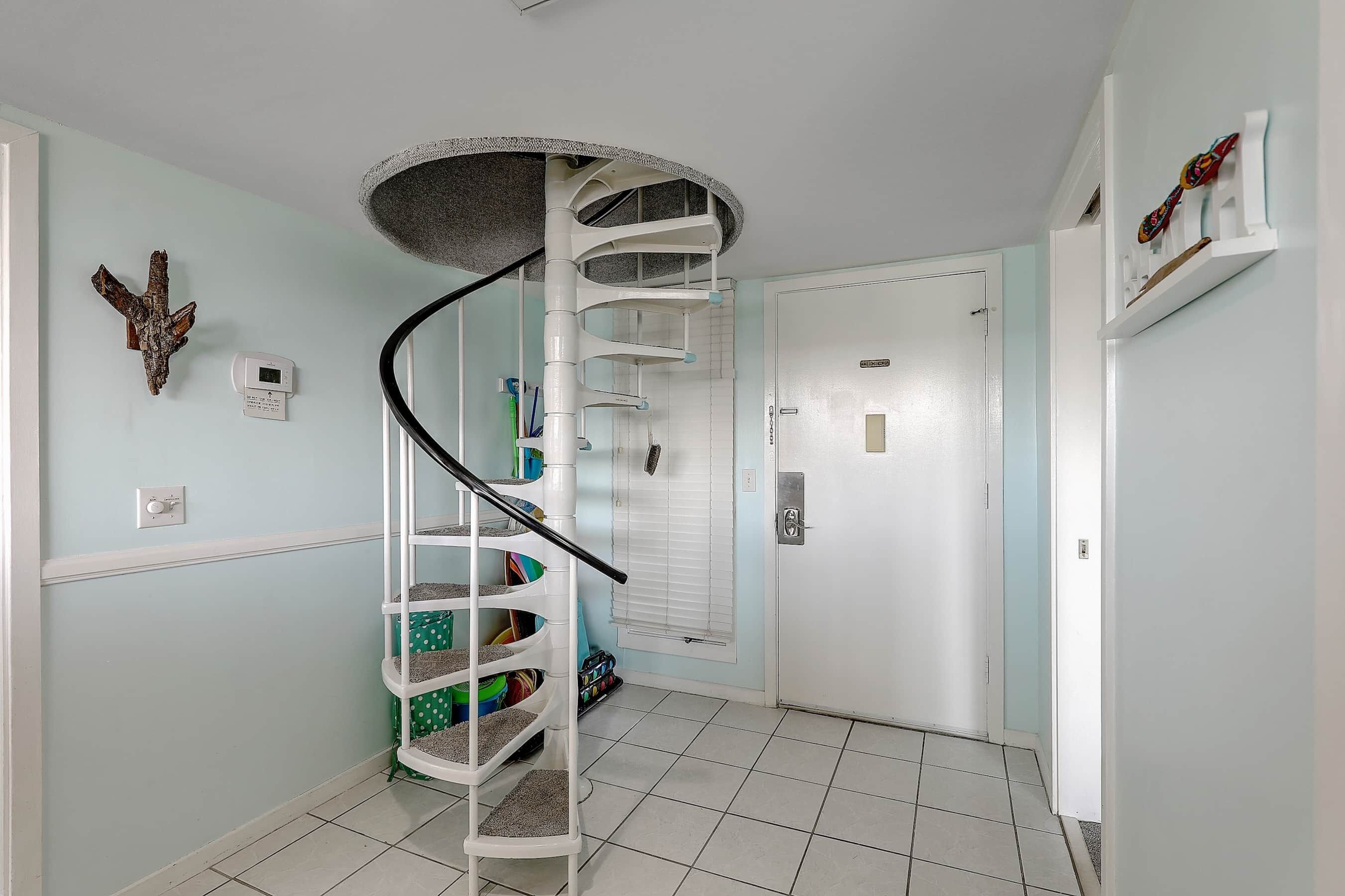 Una escalera de caracol con barandilla, una puerta con manija e interruptor de luz en la pared.