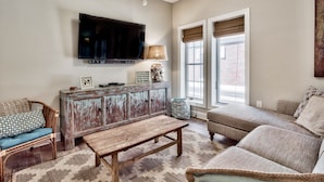 A living room with a television mounted on the wall, a wooden bench, a sofa, and a patterned rug.