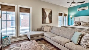 A living room with a sectional sofa, a wooden coffee table, and a large window with blinds.