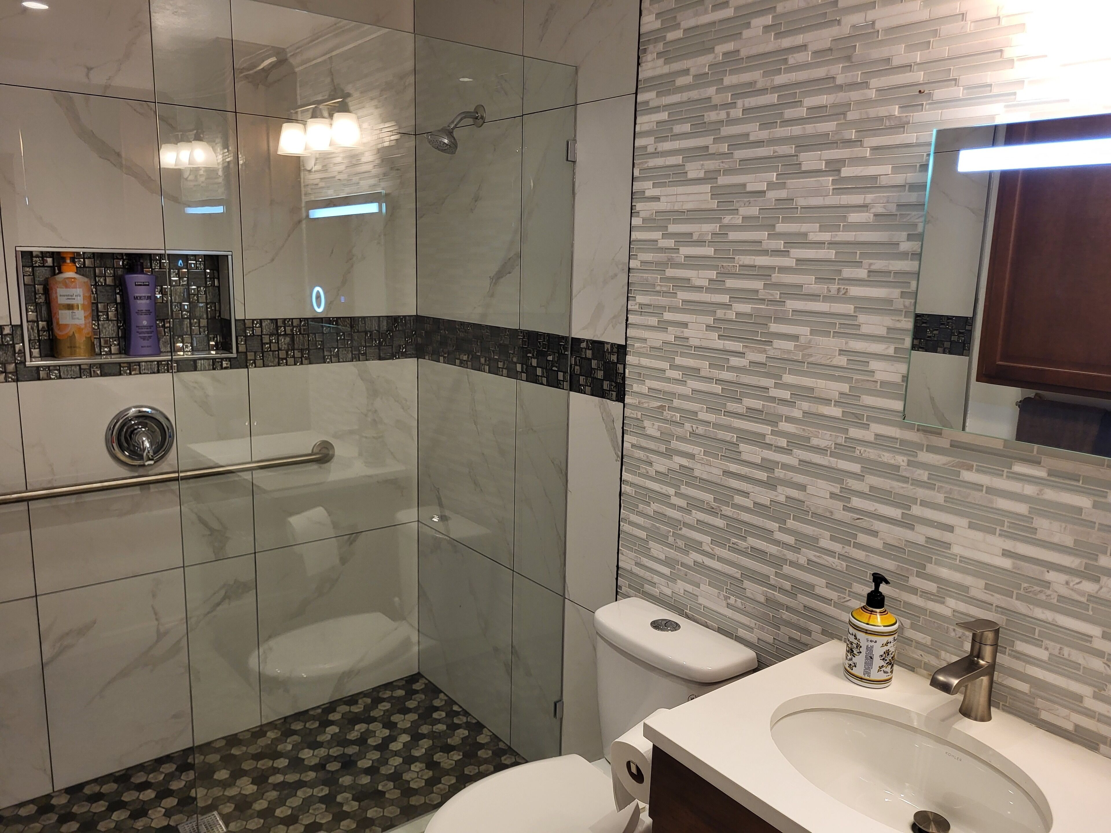 A modern bathroom with a glass shower enclosure, a toilet, and a sink with a mirror above.