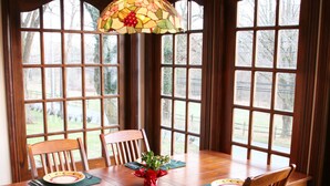 Een houten eettafel met stoelen, een hanglamp van glas-in-lood en een uitzicht door grote ramen.