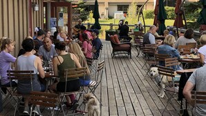 Une terrasse extérieure avec des tables et des chaises en bois, entourée de bâtiments et offrant une vue sur un paysage montagneux.