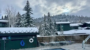 Une piscine à l’eau d’un bleu cristallin, entourée d’arbres et de bâtiments recouverts de neige.
