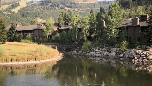 Une vue sur un lac, avec un pont, une rangée de bâtiments et un paysage vallonné en arrière-plan.