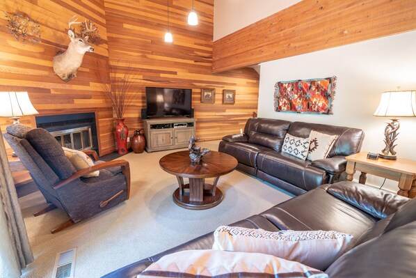 A living room with a fireplace, leather sofas, a television, and wooden paneling.