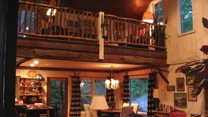 Een gezellig interieur van een chalet met een houten trap, een bank, een eettafel en een boekenkast.