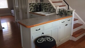 Een keuken met een houten trap, een betegelde spatwand en een barkruk met fietsmotief.