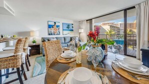 Un salon moderne avec un coin repas, doté d’une grande fenêtre offrant une vue sur les palmiers et les immeubles.