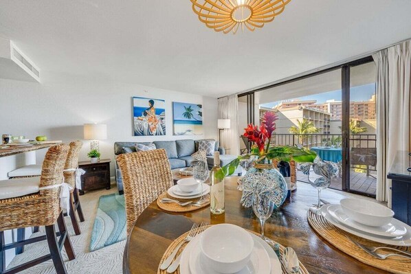 A modern living room with a dining area, featuring a large window with a view of palm trees and buildings.
