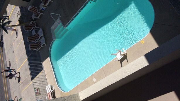Vue aérienne d’une piscine avec un plongeoir, entourée de chaises longues et d’un panneau indiquant « Interdiction de plonger ».