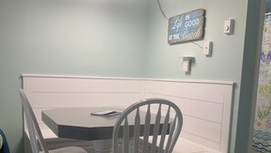 Un coin repas comprenant une table ronde, deux chaises blanches, un banc et un luminaire fixé au mur.