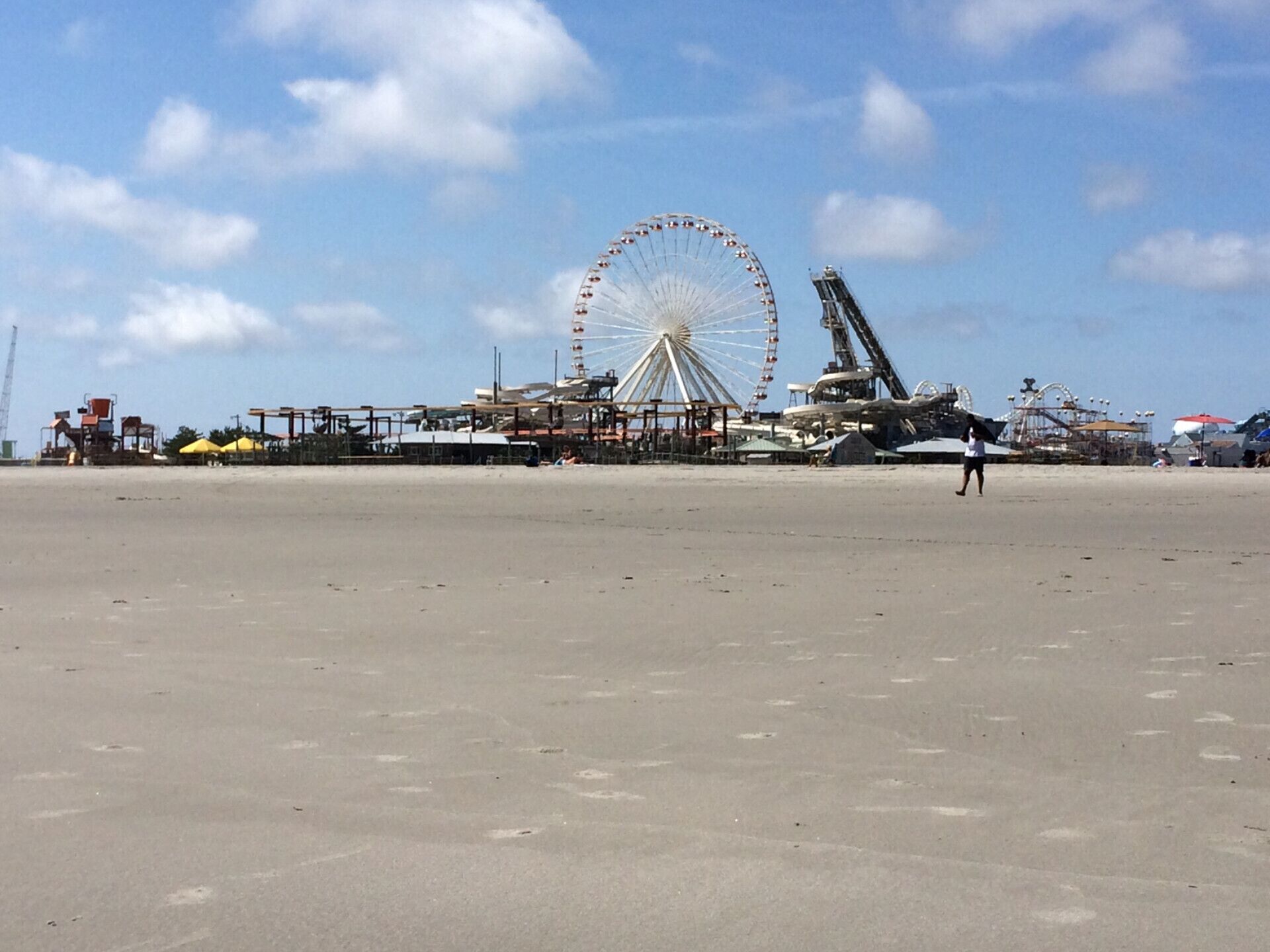 Uma praia com uma grande roda-gigante e atrações de parque de diversões ao fundo.