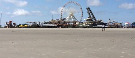 Uma praia com uma grande roda-gigante e atrações de parque de diversões ao fundo.
