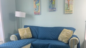 Une pièce avec un canapé bleu, un pouf à rayures et deux coussins. Trois œuvres d’art sont accrochées au mur au-dessus du canapé.