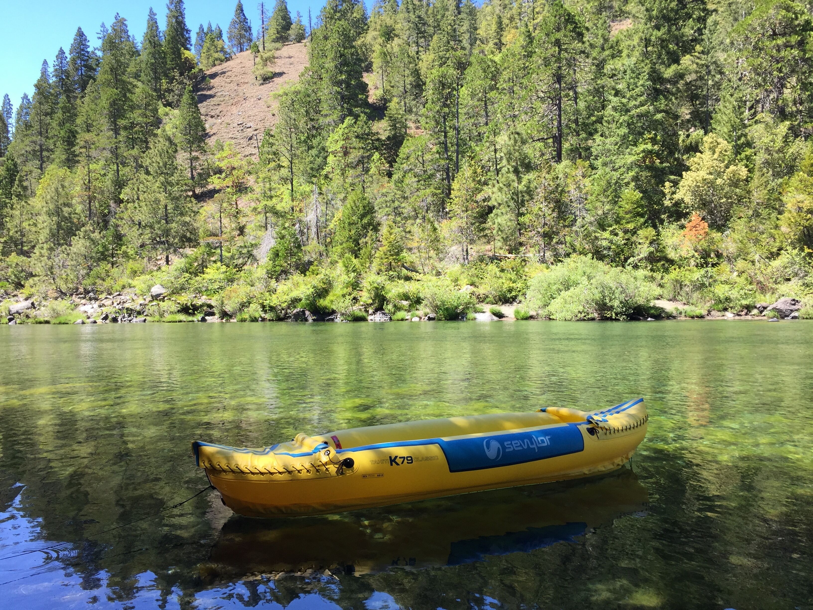 Un bote inflable amarillo sobre un río tranquilo, rodeado de un bosque frondoso.